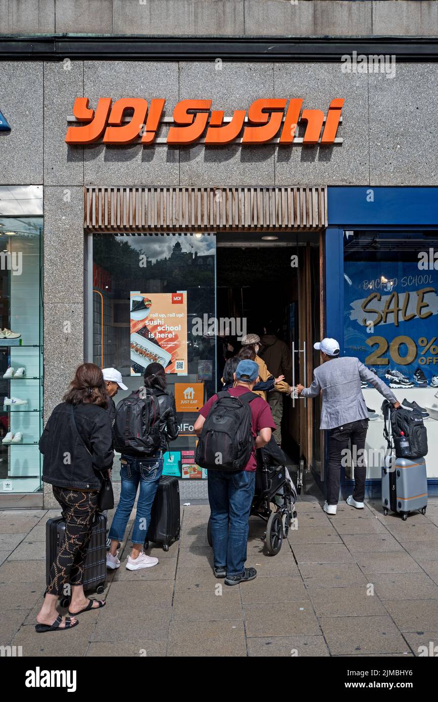 Einige Leute mit Koffern gehen in eine Zweigstelle von YO! Sushi in der Princes Street, Edinburgh, Schottland, Großbritannien. Stockfoto