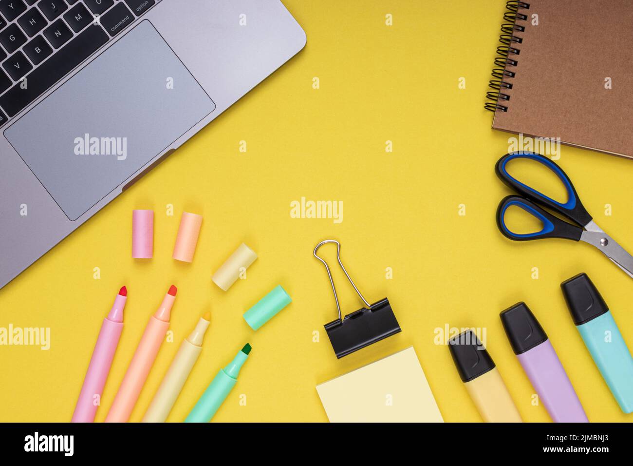 Laptop, Schere, Klemme, Notizblock, Buntstifte. Zurück zur Schule. Isolierter gelber Hintergrund Stockfoto