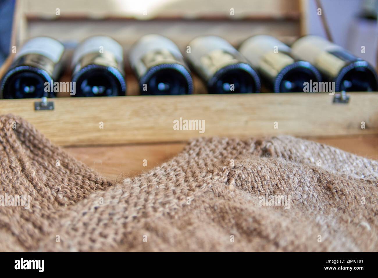 Holzkiste aus Rotweinflaschen mit einem handgefertigten braunen Poncho auf der Vorderseite. Besuch einer Weinkellerei in mendoza, argentinien. Selektiver Fokus Stockfoto