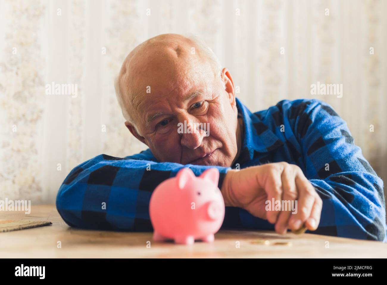 Trauriger, verlorener und deprimierter kaukasischer älterer Mann, der mit einem Sparschwein auf dem Tisch lag und seine letzten Münzen zählte. Hochwertige Fotos Stockfoto