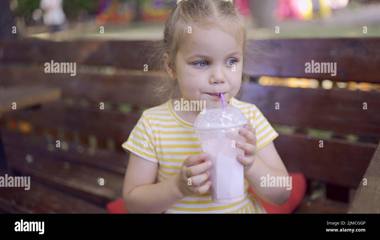 Das kleine Mädchen trinkt einen Milchshake durch einen Strohhalm. Nahaufnahme Porträt von niedlichen Mädchen auf Parkbank sitzen und trinken Milchshake. Odessa, Ukraine Stockfoto