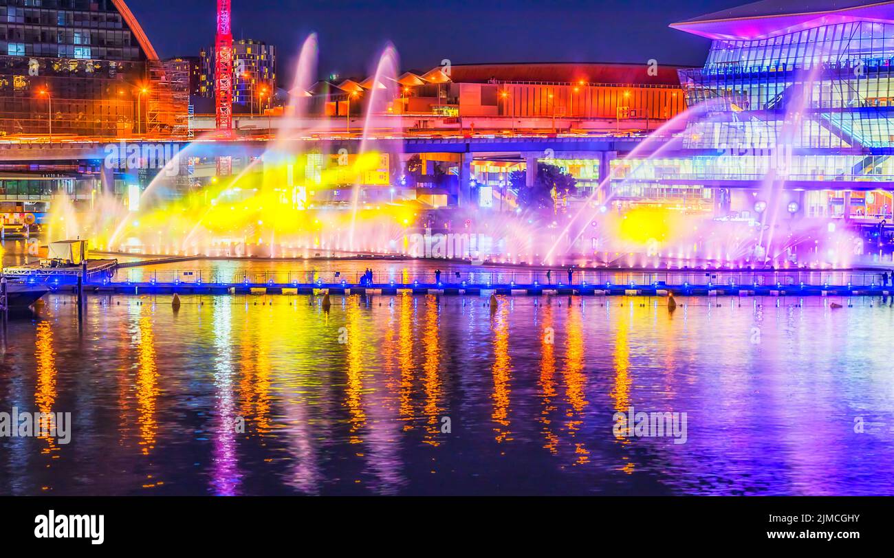 Malerische farbenfrohe Wasserfontänen an der Coockle Bay im Darling Harbour Dining District von Sydney City bei Sonnenuntergang mit heller Beleuchtung. Stockfoto