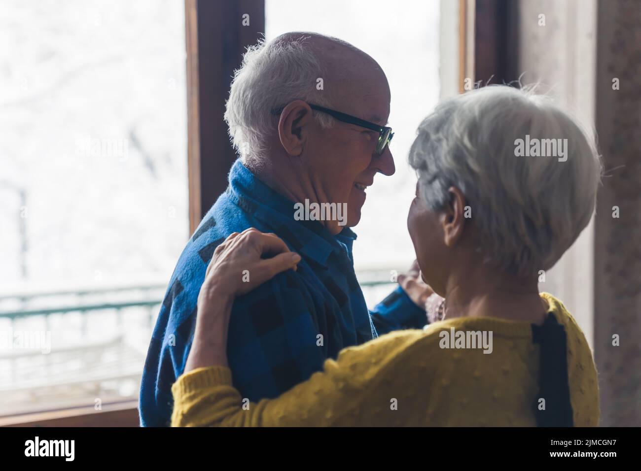 Süßes älteres europäisches Ehepaar, das im Wohnzimmer lacht und tanzt, die Hände hält und an kalten Wintertagen Zeit miteinander verbringt. Hochwertige Fotos Stockfoto