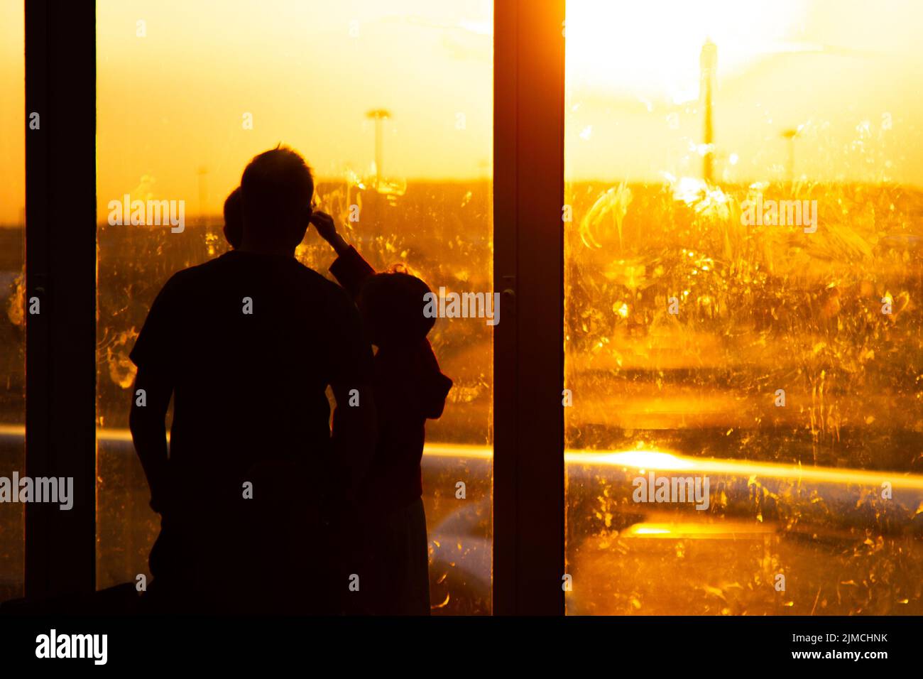 Familie, die während des Sonnenuntergangs aus einem Fenster auf Flugzeuge auf einen Luftport schaute und auf ihr Flugzeug wartete Stockfoto