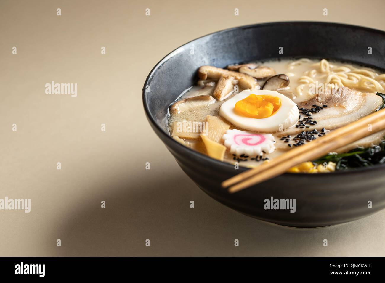 Von oben appetitlich japanischer Ramen mit gekochtem Ei und Pilzen serviert in einer Schüssel mit hölzernen Essstäbchen auf beigem Hintergrund Stockfoto