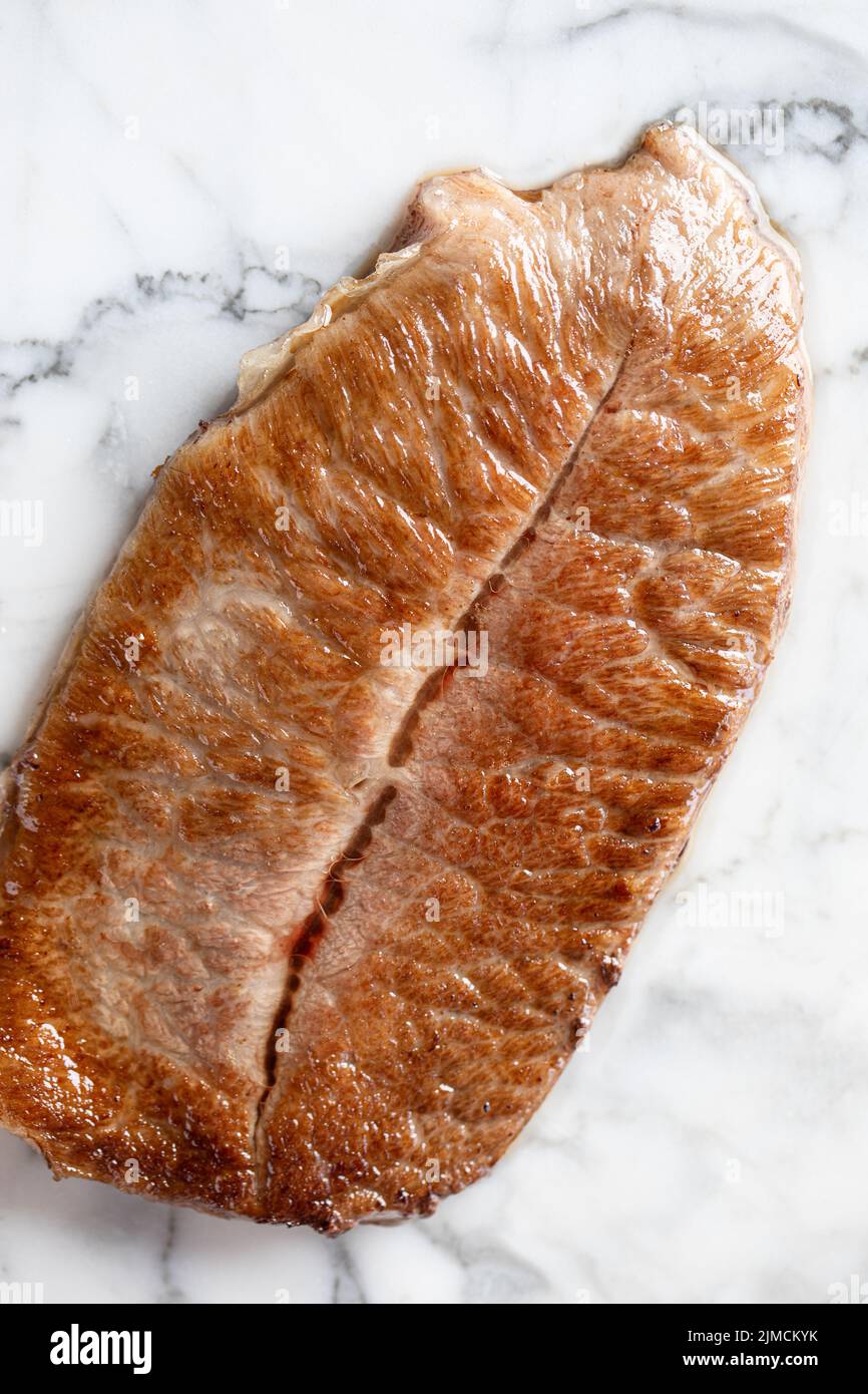 Blick von oben auf das schmackhafte wagyu-Rindfleisch der Präfektur kobe, das während des Kochvorgangs auf einem Schneidebrett aus Marmor in der hellen Küche serviert wird Stockfoto