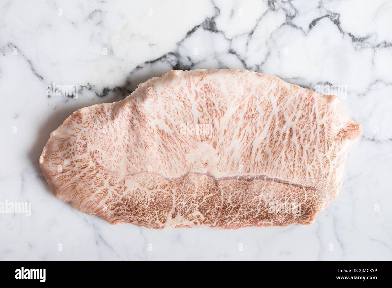 Blick von oben auf das traditionelle japanische, ungekochte wagyu-Rindfleisch der Präfektur kobe, das während der Zubereitung auf einem Marmortisch im hellen Raum aufgestellt wurde Stockfoto