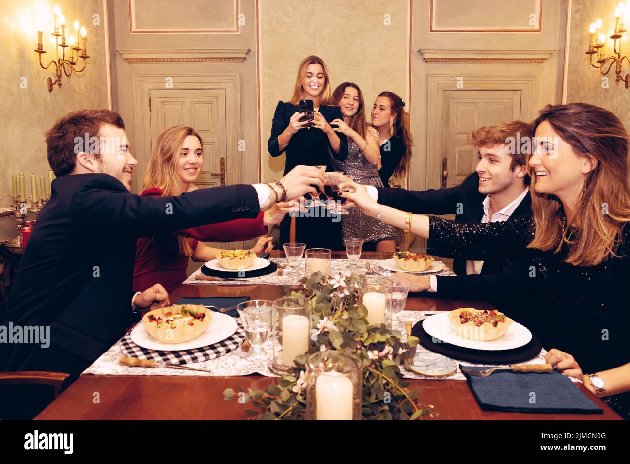 Gruppe positiver Freunde, die sich gegenseitig anguckten und beim Abendessen im Restaurant mit Weingläser am Tisch mit leckerem Essen toasten Stockfoto