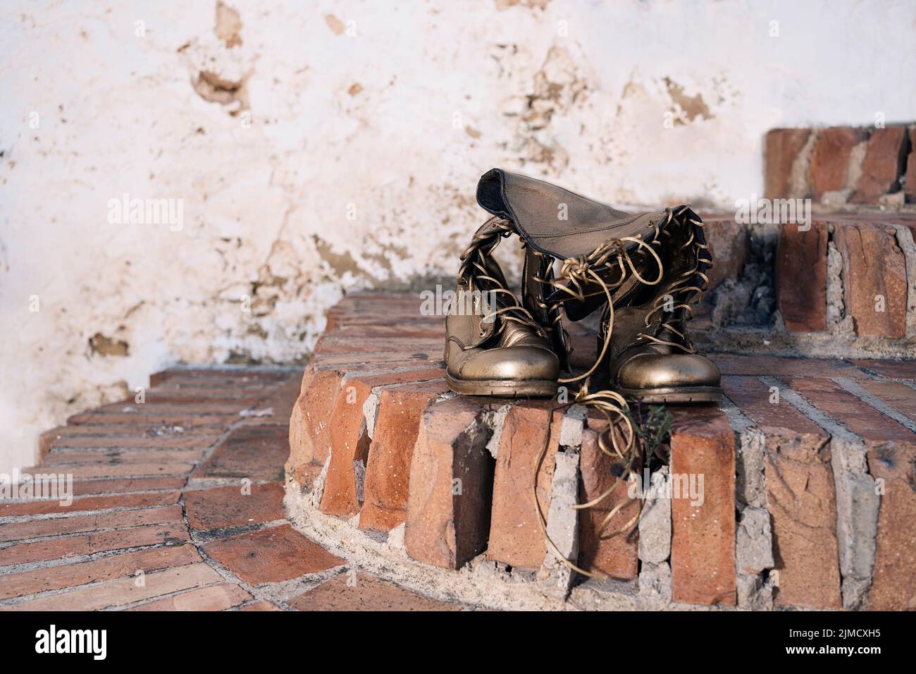 Bronzefarbene Stiefel mit Schnürsenkeln, die an sonnigen Tagen auf der Straße auf schäbigen Ziegeltreppen platziert sind Stockfoto