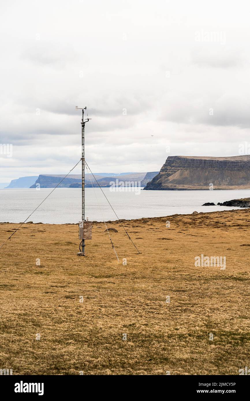 Kleine Wetterstation, die auf einem Mast an grasbewachsenen Küsten in der Nähe des Meeres gegen Berge im Küstengebiet Islands in der Natur montiert ist Stockfoto