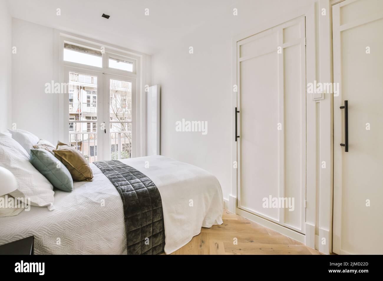 Modernes, weißes und beleuchtetes Schlafzimmer mit großem Bett, Schrank und minimaler Dekoration und Möbeln Stockfoto