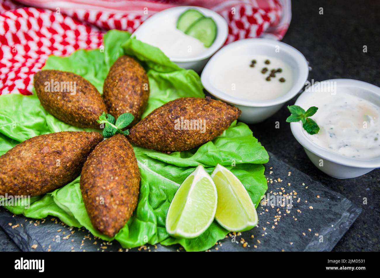 Köstliche libanesische Gerichte, Kibbeh (Kibe) mit Saucen und Zitrone auf schwarzem Schiefer und Granitrückstand Stockfoto