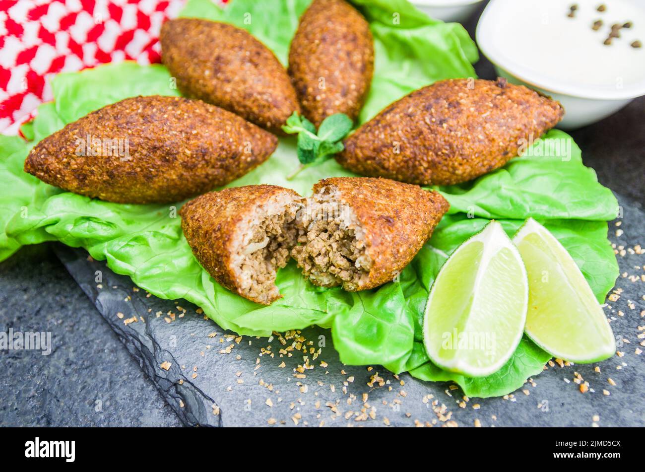 Köstliche libanesische Gerichte, Kibbeh (Kibe) mit Saucen und Zitrone auf schwarzem Schiefer und Granitrückstand Stockfoto