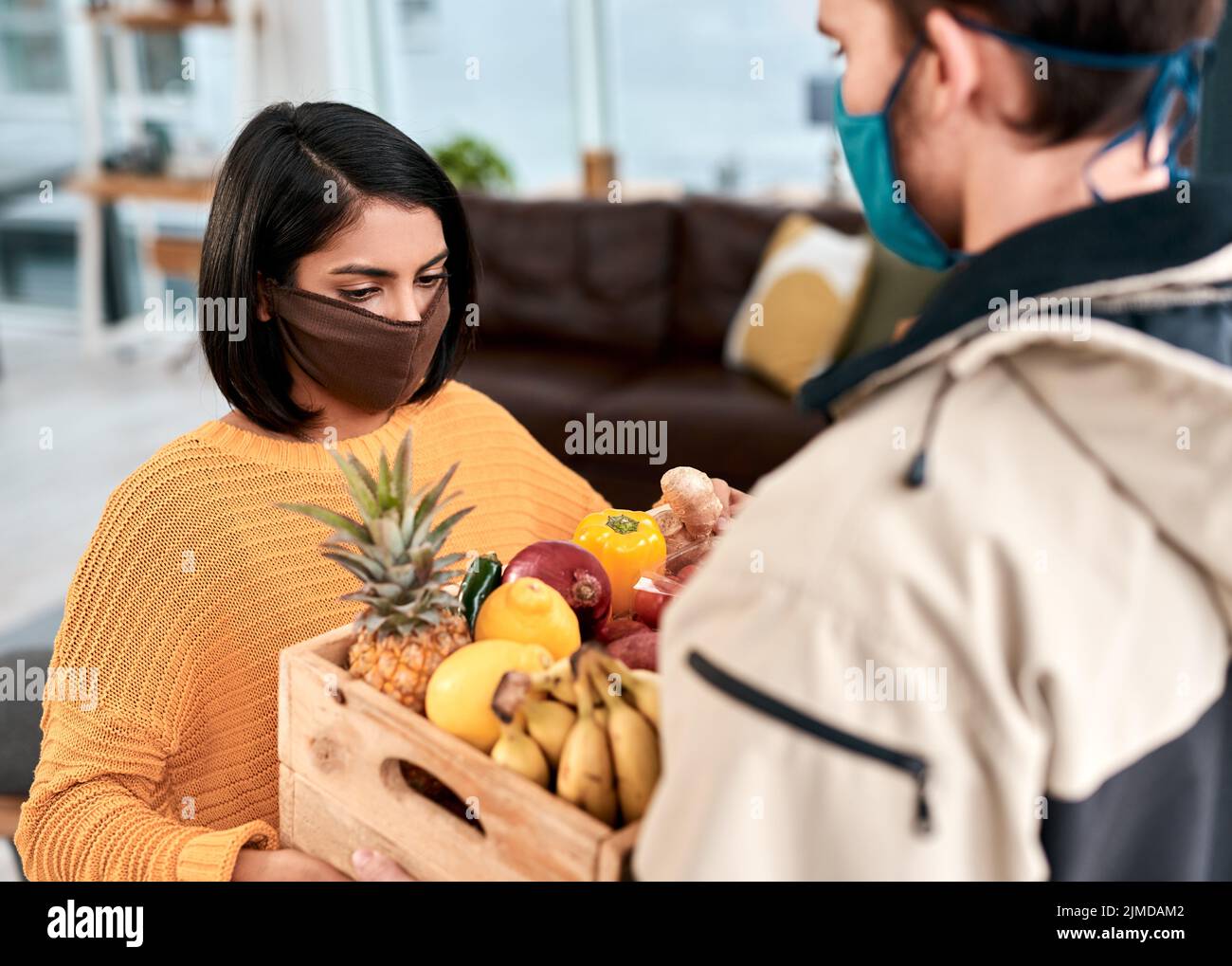 Das Geschäft mit der Hauszustellung boomt während der Sperrung. Eine maskierte junge Frau erhält eine Lieferung von frischem Obst und Gemüse zu Hause. Stockfoto