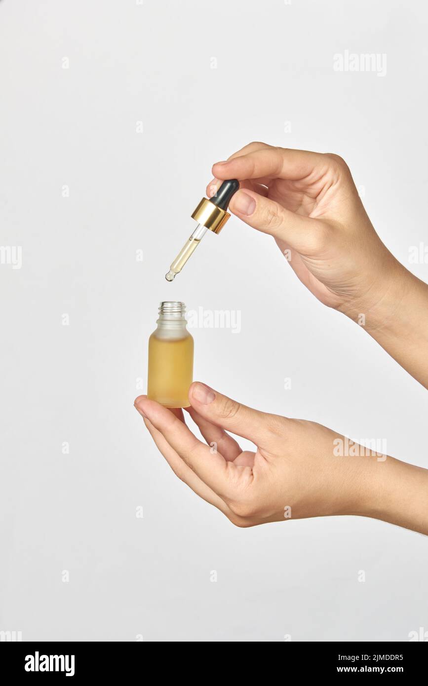 Flasche und Pipette von medizinischem Cannabis CBD-Öl in den Händen vor hellgrauem Hintergrund. Stockfoto