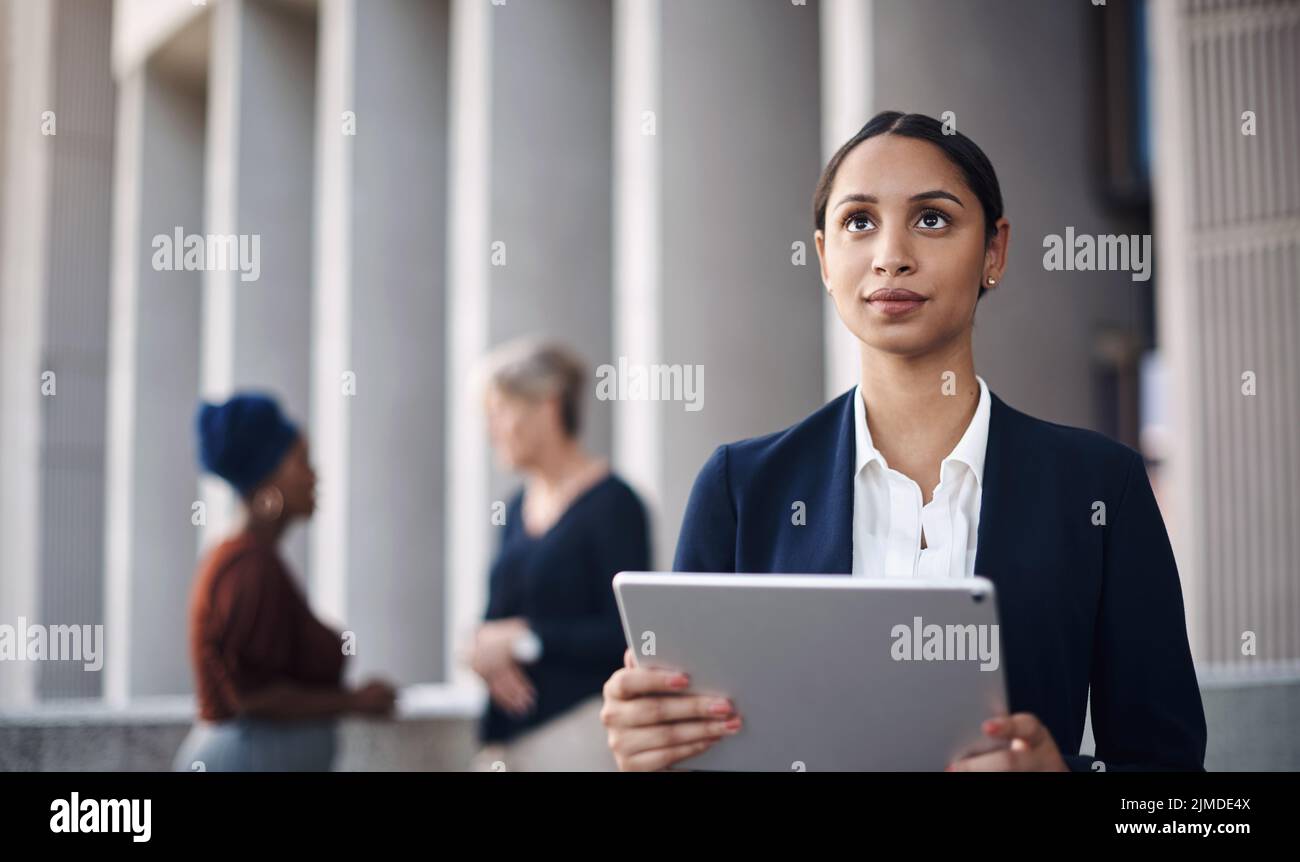 Machen Sie es möglich, wo immer Sie gerade sind: Eine junge Geschäftsfrau, die ein digitales Tablet vor einem Hintergrund der Stadt nutzt. Stockfoto