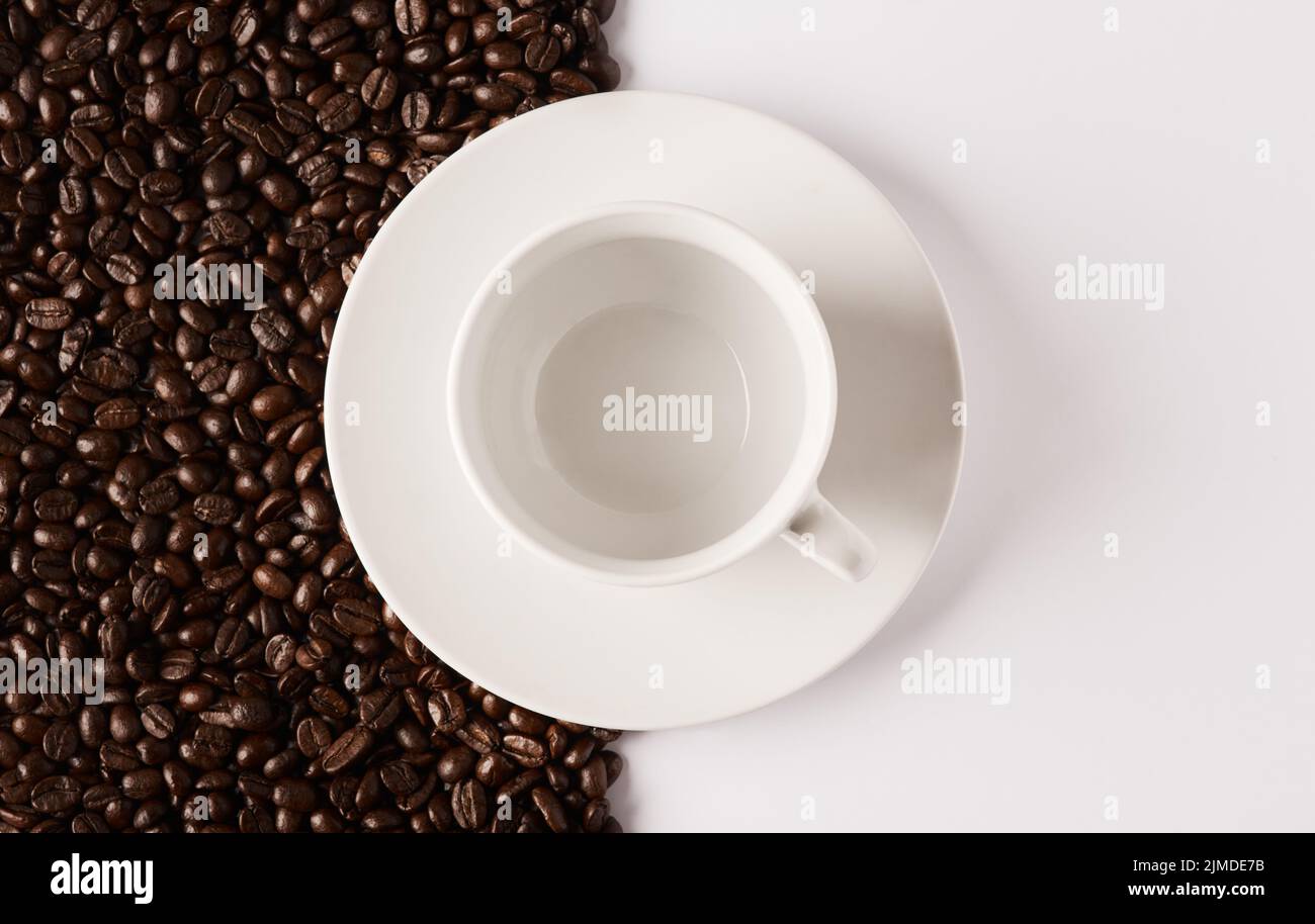 Zum Kaffee oder nicht zum Kaffee... Nahaufnahme einer leeren Tasse und Untertasse vor einem halb-und-halb Hintergrund von Kaffeebohnen. Stockfoto