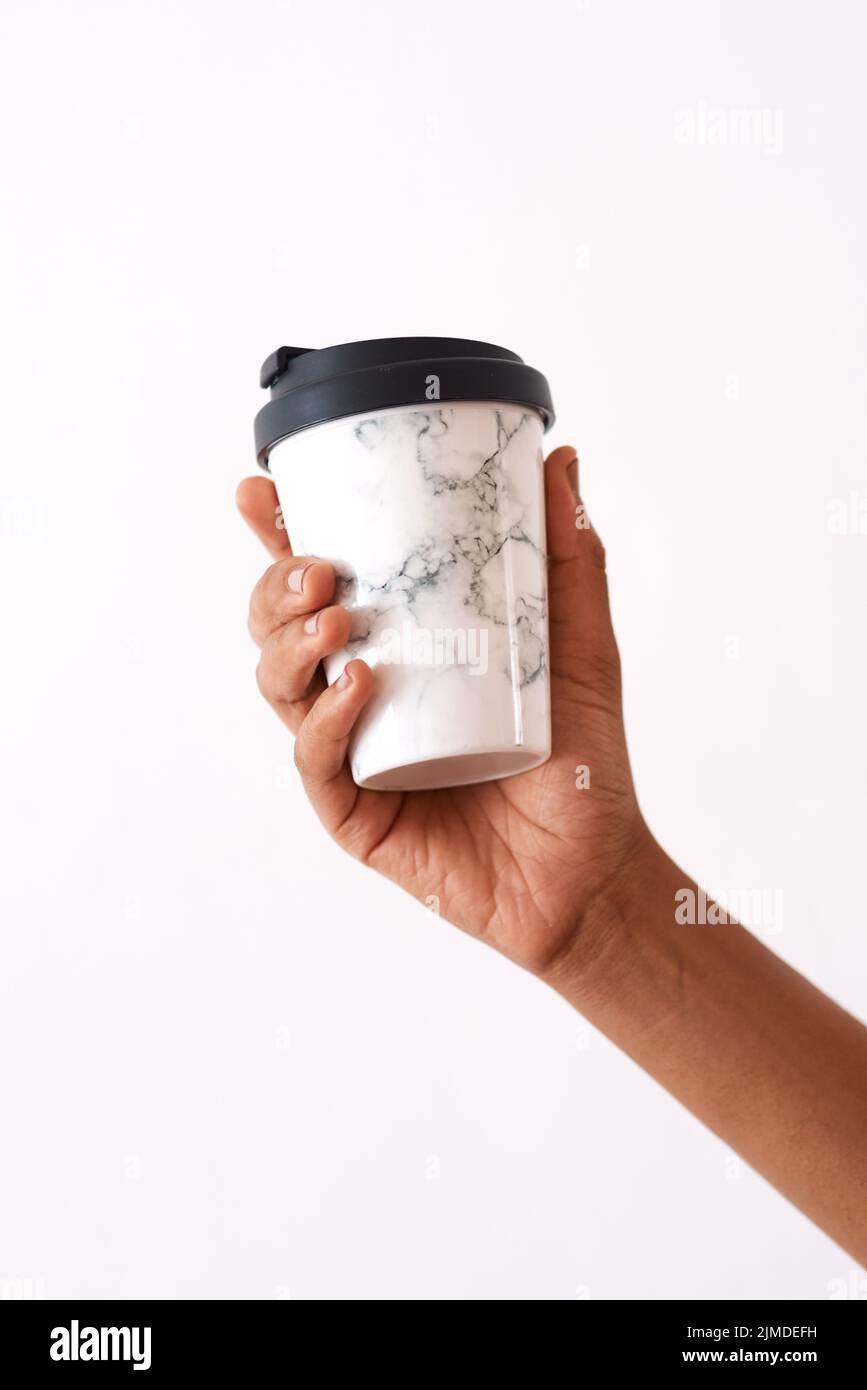 Ein Kaffee macht alle Sorgen Geh weg. Studioaufnahme einer nicht erkennbaren Frau, die eine wiederverwendbare Kaffeetasse vor einem weißen Hintergrund hält. Stockfoto