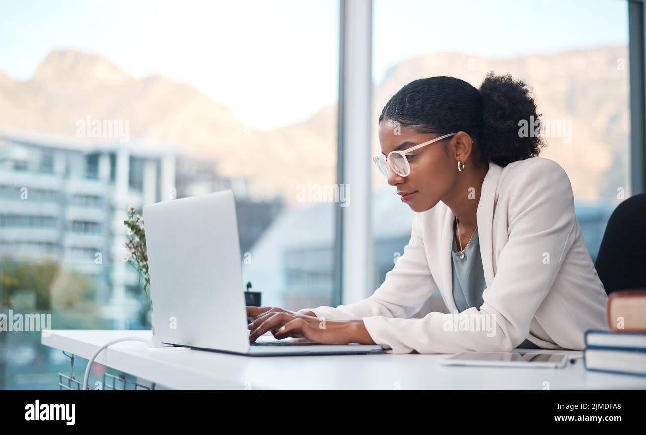 Datenfachkraft und Sekretärin schreiben eine E-Mail auf einen Laptop und recherchieren online, während sie in einem Büro arbeiten. Afrikanischer Unternehmer, der konzentriert aussieht Stockfoto