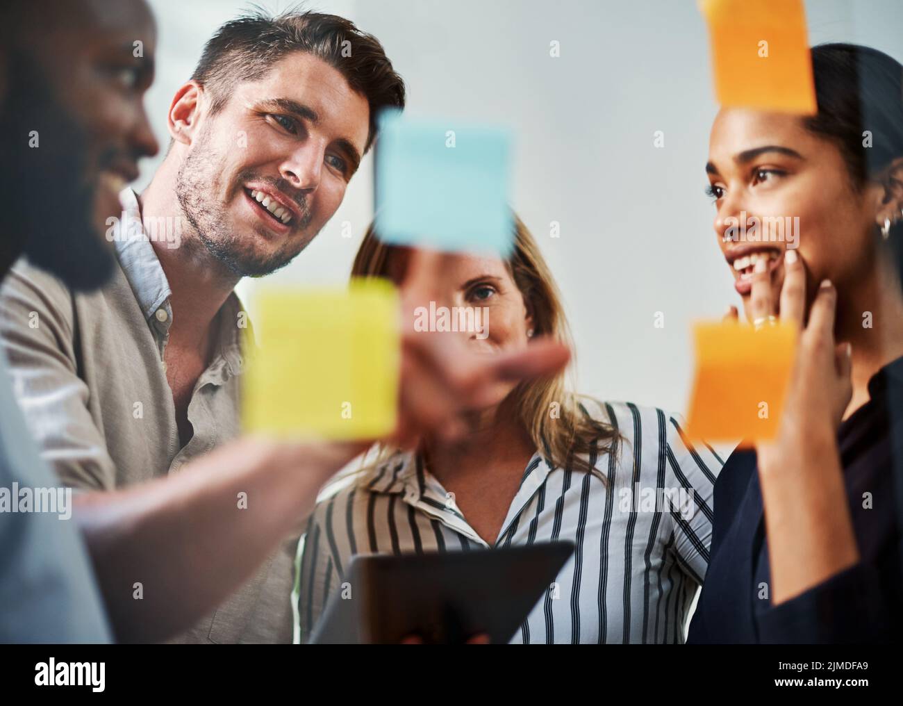 Sie sind ein Team, das erfolgreich ist. Eine Gruppe von Geschäftskollegen, die in ihrem Büro auf einem Glaswischbrett Brainstorming durchführen. Stockfoto