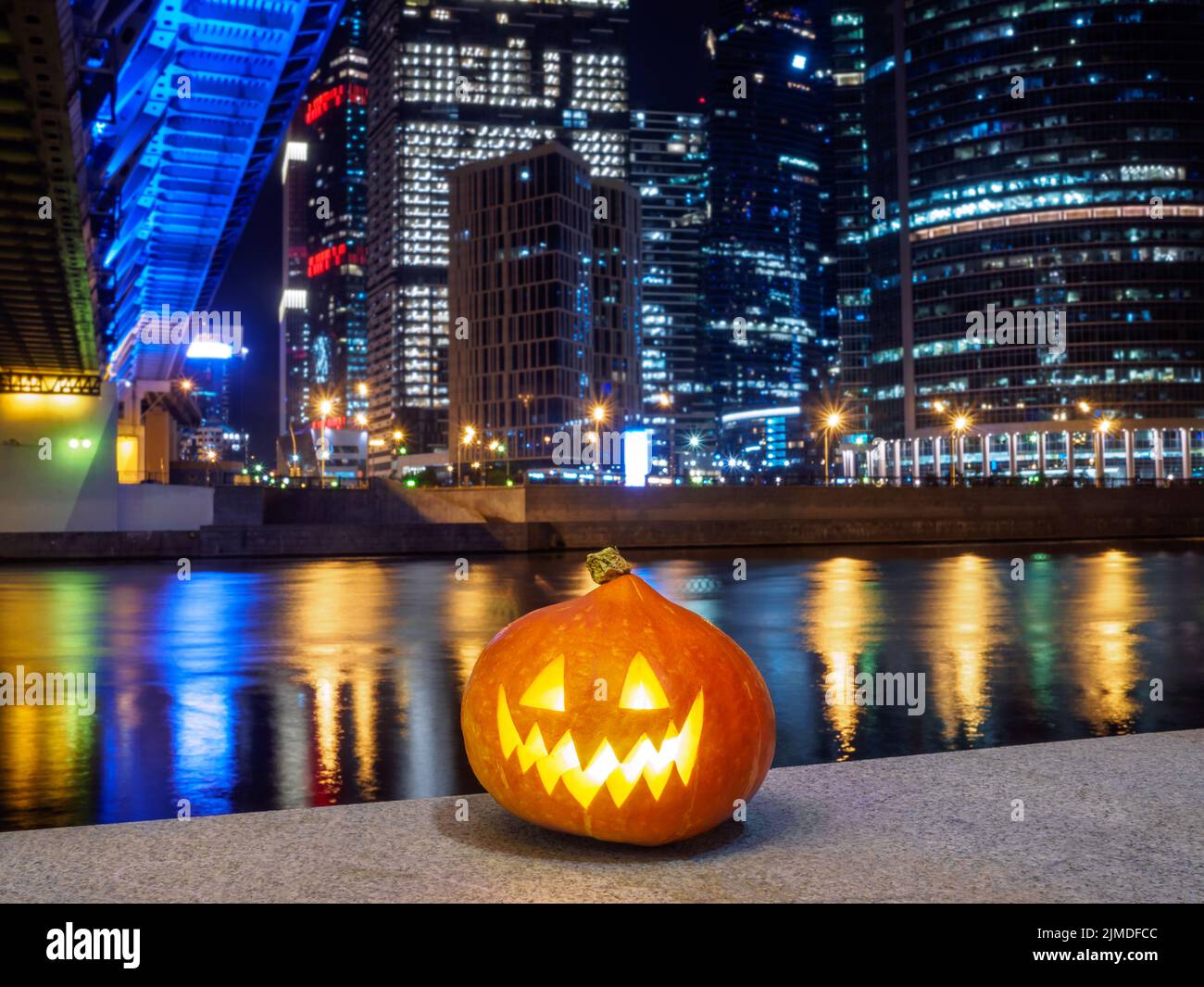 Halloween Kürbis auf dem Hintergrund der Nachtstadt. Mehrstöckige Gebäude und Wolkenkratzer. Verschwommene farbige Lichter werden reflektiert Stockfoto