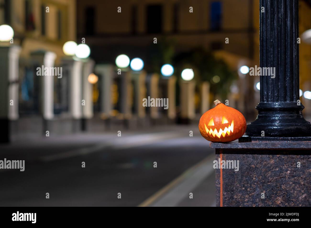 Halloween Kürbis auf einer verlassenen Stadtstraße in der Nacht. Die Lichter der Stadt und die alten Hochhäuser sind in verschwommenen Farben. Stockfoto