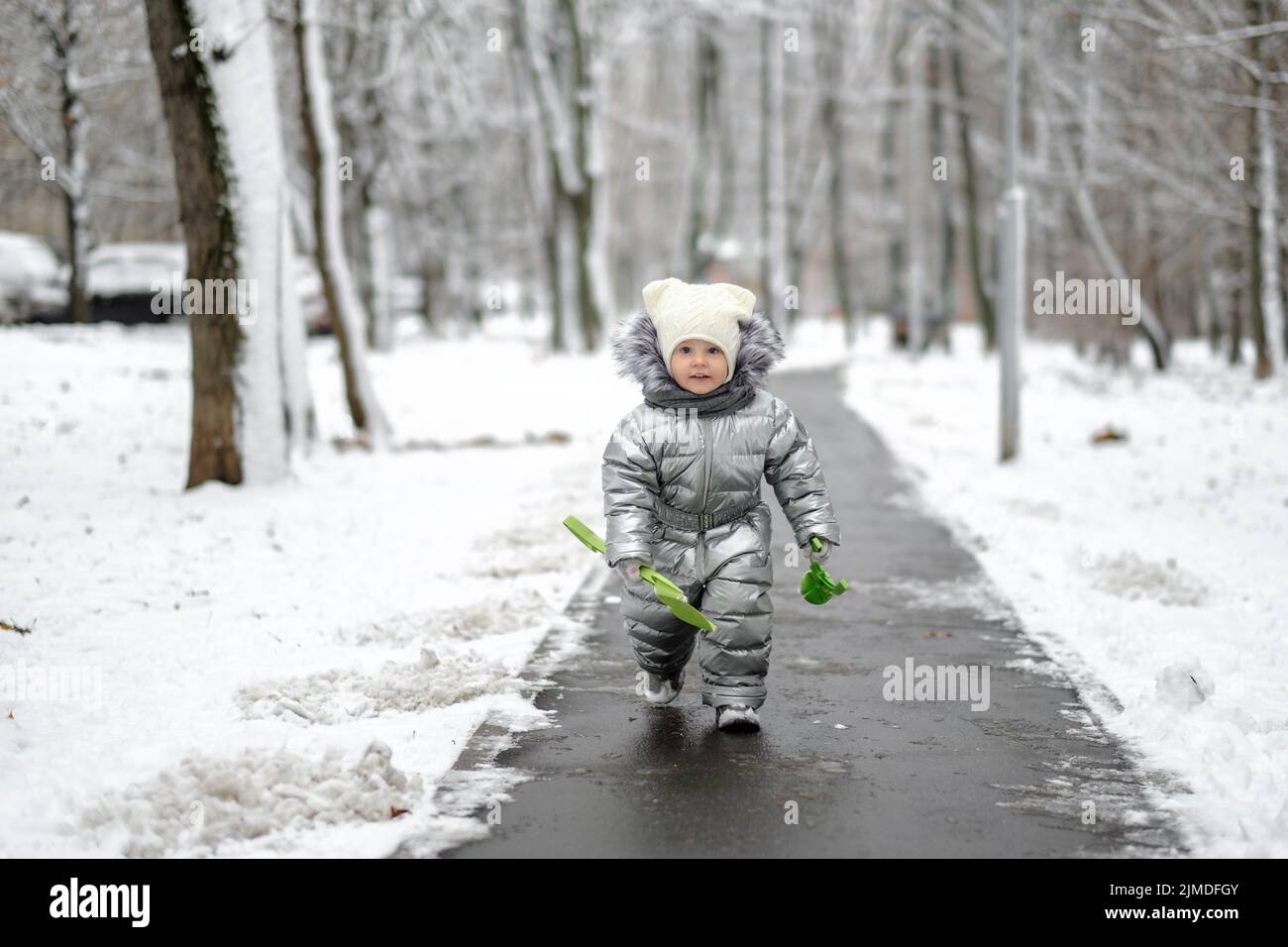 Ein lustiges Mädchen in einem warmen silbernen Jumpsuit läuft im Winter den Weg entlang. Stockfoto