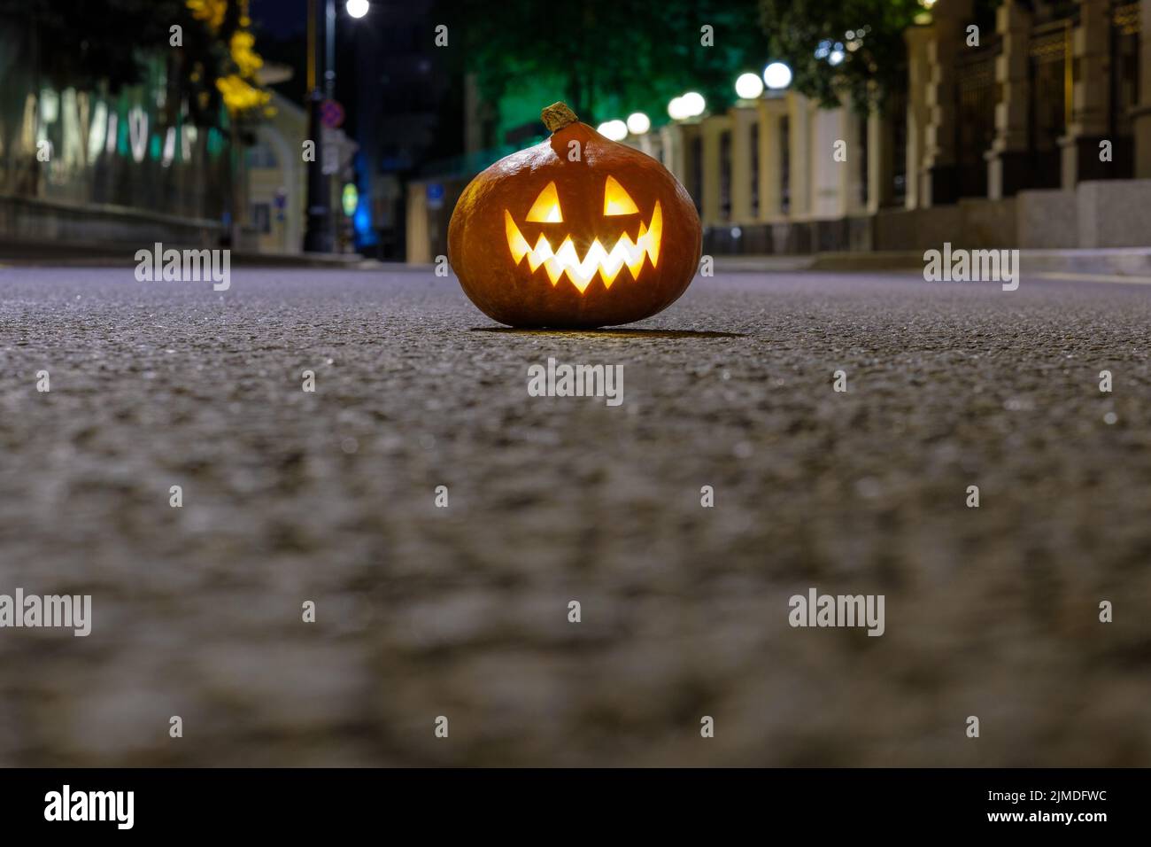 Halloween Kürbis auf dem Asphalt auf einer verlassenen Stadtstraße in der Nacht. Verschwommene farbige Lichter der Stadt und alte Gebäude. Stockfoto