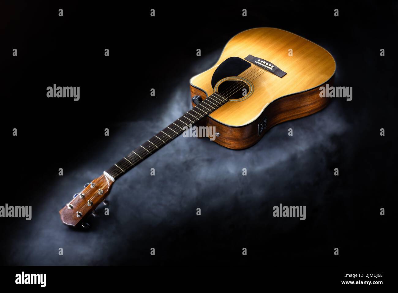 Akustische 6-saitige Gitarre in klassischer gelber Farbe auf isoliertem schwarzem Hintergrund, umgeben von Nebel Stockfoto