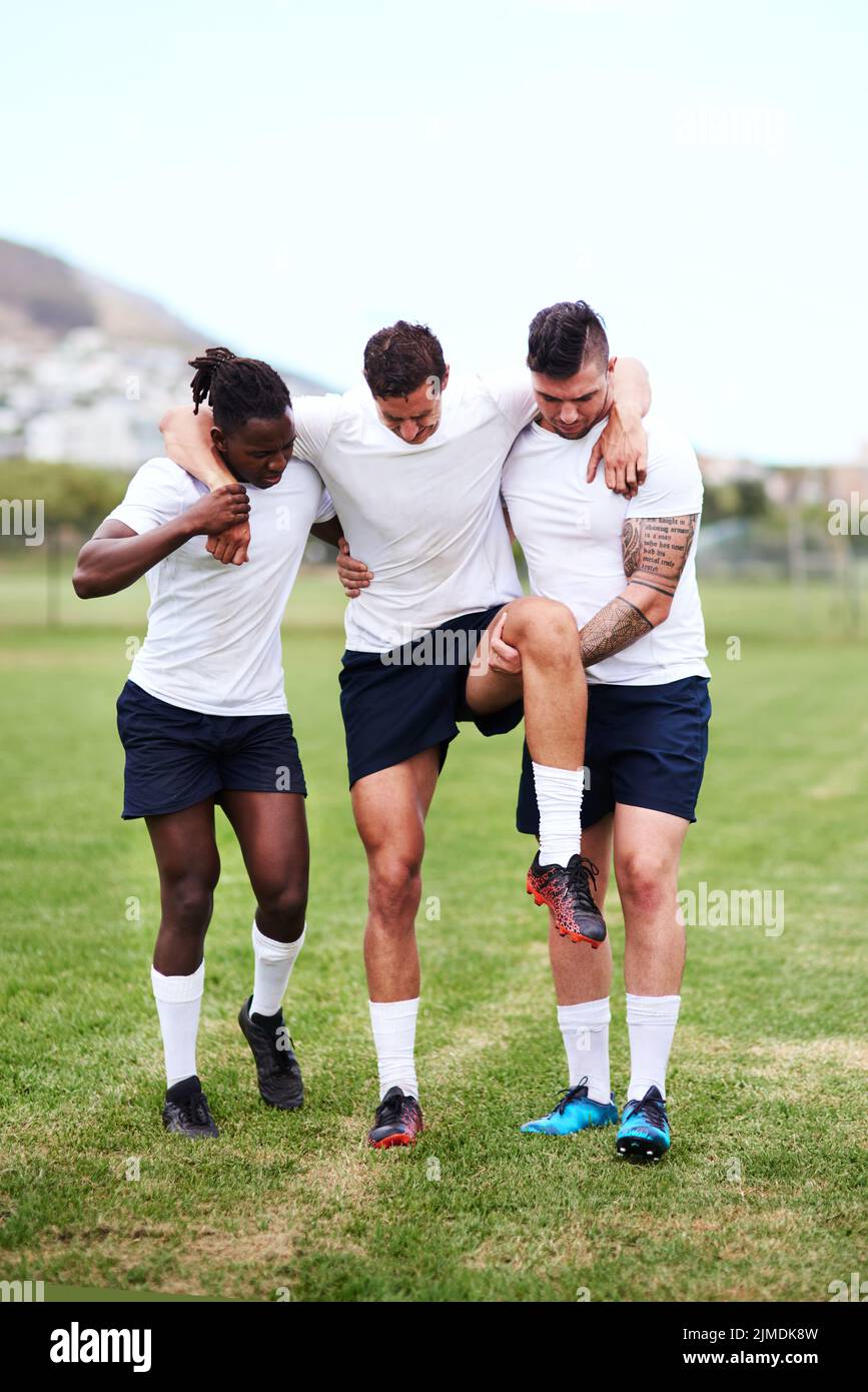 Wie Soldaten, die aus dem Krieg zurückkehren. Junge Männer tragen ihren Mannschaftskollegen vom Spielfeld, nachdem sie sich während eines Rugby-Spiels sein Knie verletzt haben. Stockfoto