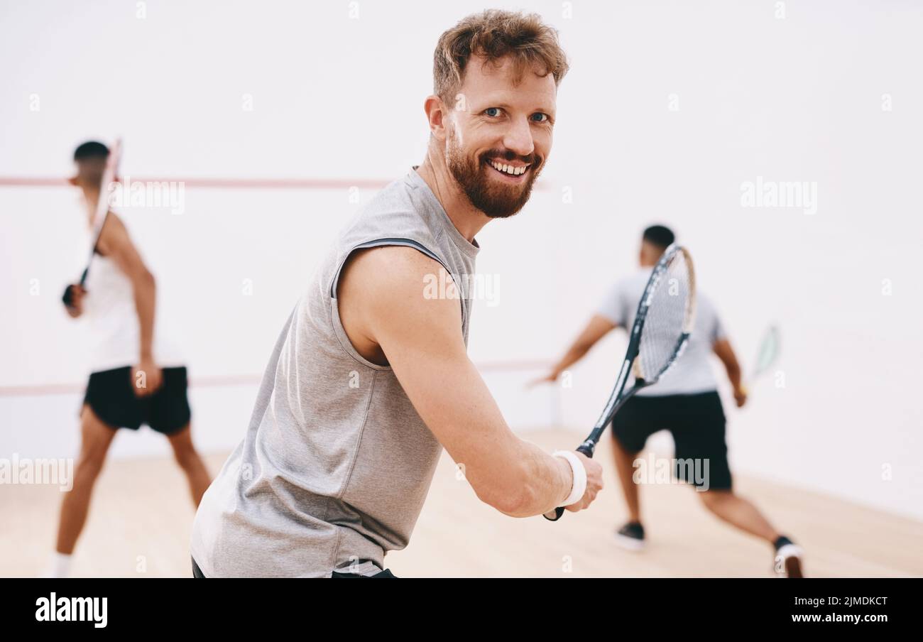 Seht zu, wie ich mit dem Ball Magie mache. Porträt eines jungen Mannes, der mit seinen Teamkollegen im Hintergrund ein Squashspiel spielt. Stockfoto