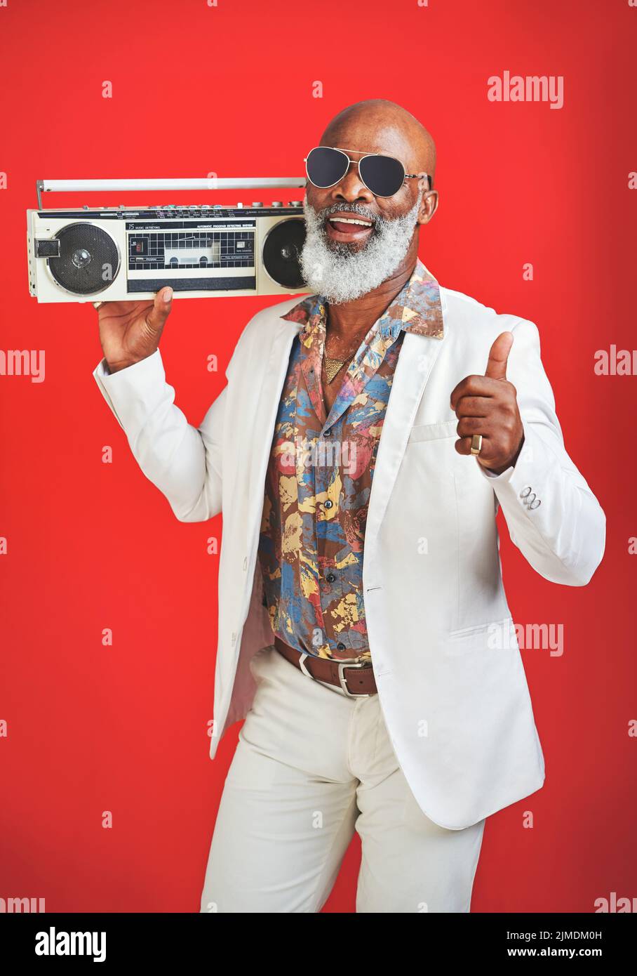 Musik ist das, was den Geist erhebt. Studioaufnahme eines älteren Mannes, der Vintage-Kleidung trägt, während er mit einer Boombox vor einem roten Hintergrund posiert. Stockfoto