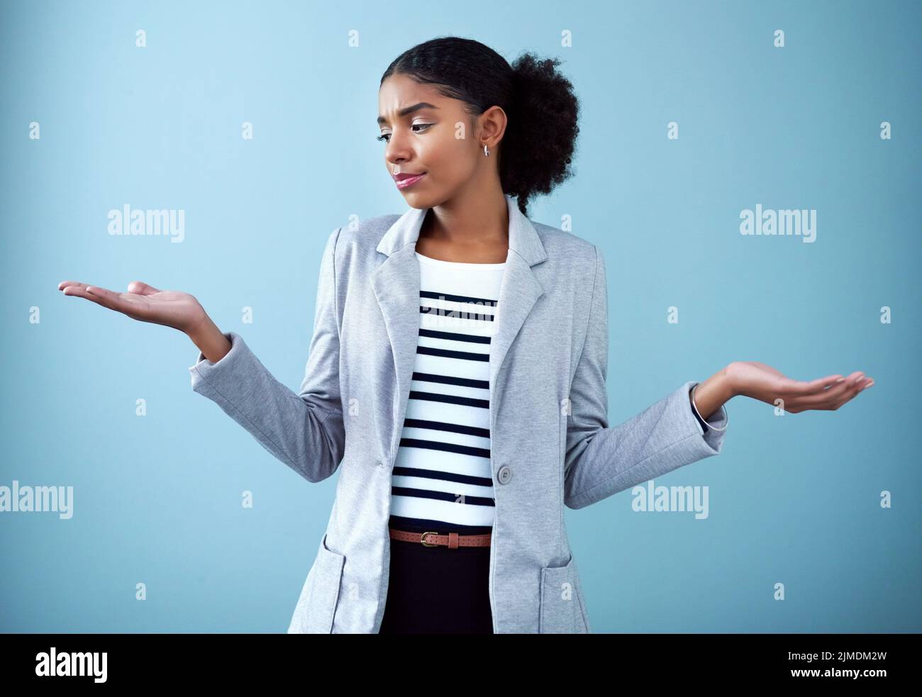 Verwirrt und seriös Geschäftsfrau mit offenen Händen oder Handflächen Emoji Pose eine schwierige Entscheidung über die zukünftige Karriere auf blauem Hintergrund. Unsicher Stockfoto