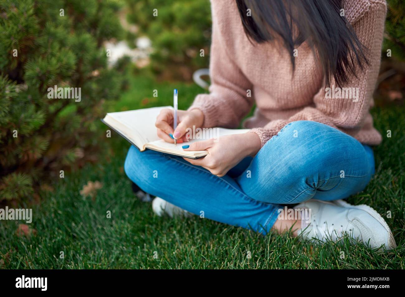 Unbekannte langhaarige Frau, die in einem Notizbuch an frischer Luft schreibt Stockfoto