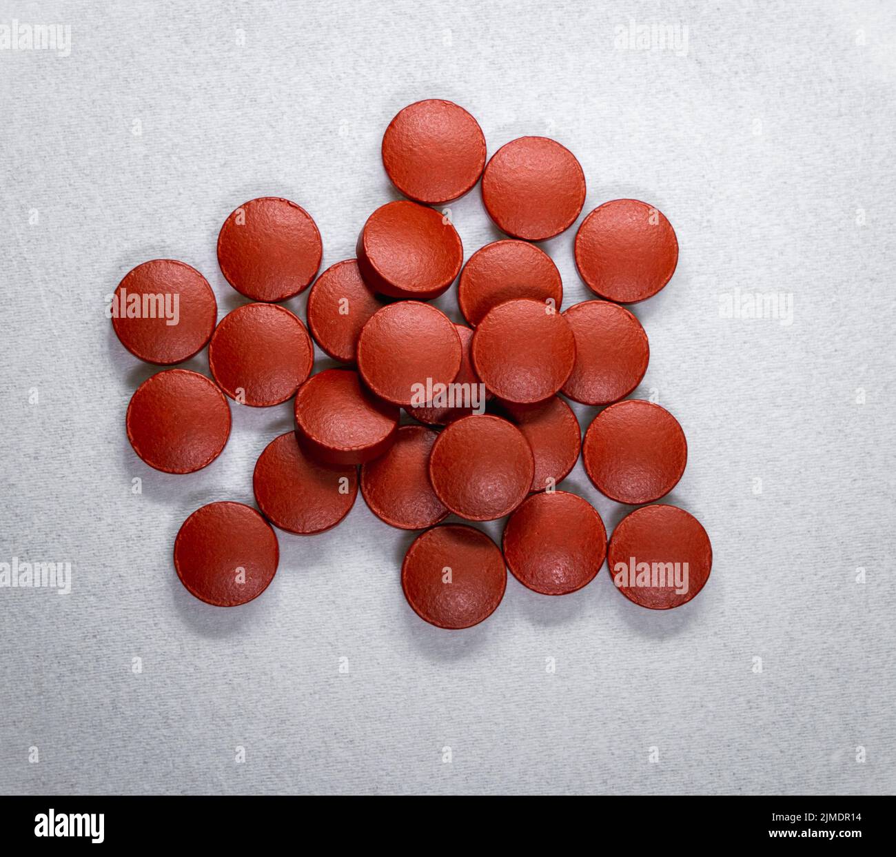 Draufsicht auf einen Haufen von roten oxideisenfarbenen Vitamin-B12-Tabletten auf einem weißen Stoffhintergrund. Stockfoto