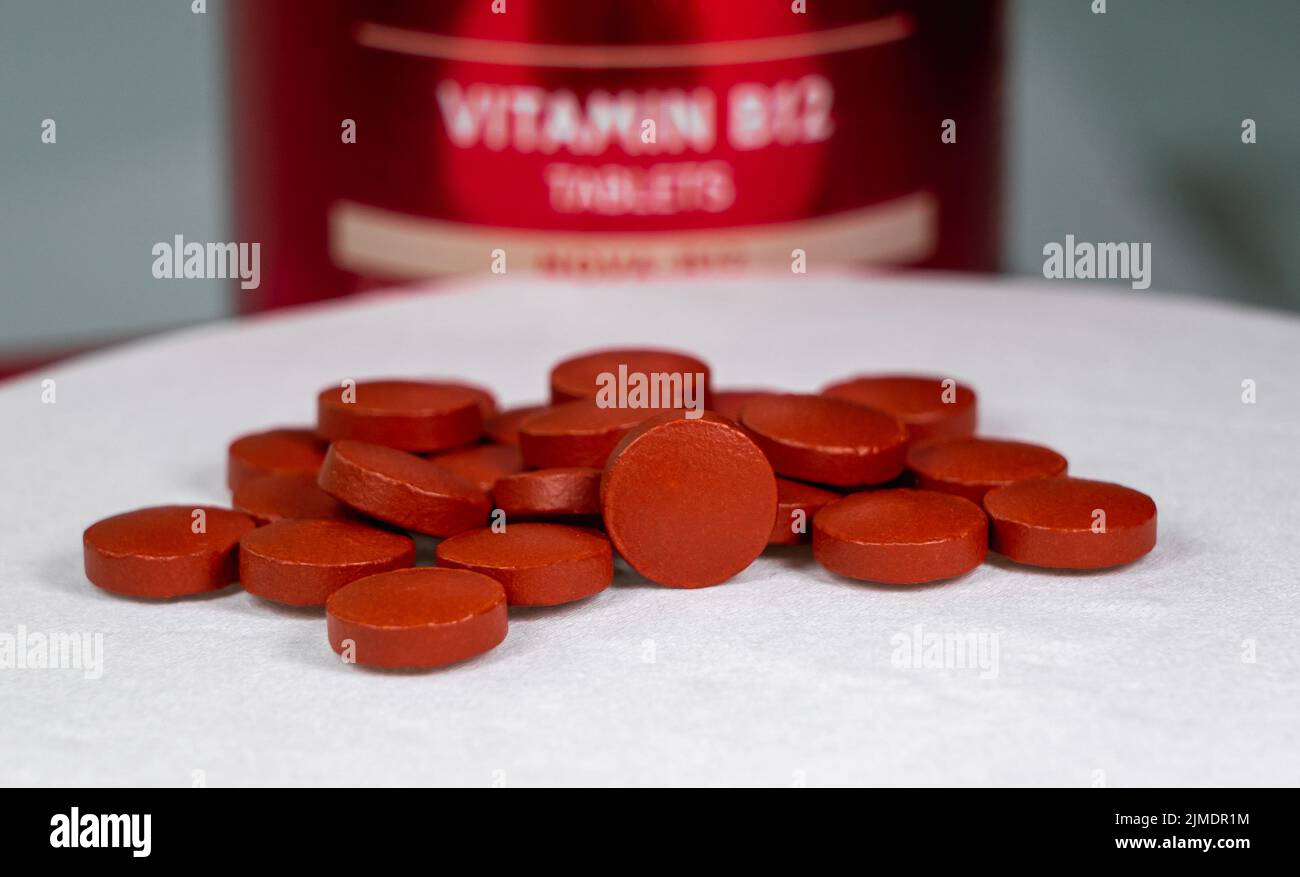 Ein Stapel von roten oxideisenfarbenen Tabletten auf einem weißen Tuch. Vitamin B12 verschwimmt im Hintergrund. Stockfoto