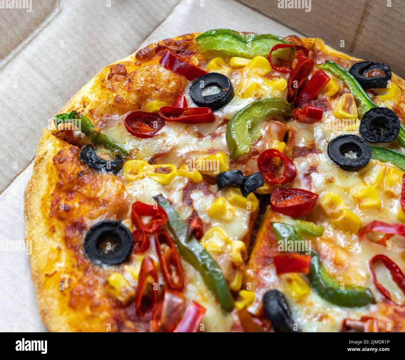 Vegetarische Pizza mit schwarzen Oliven, grünen Paprika, rotem Paprika und goldenem Mais in einer Takeout-Box. Stockfoto