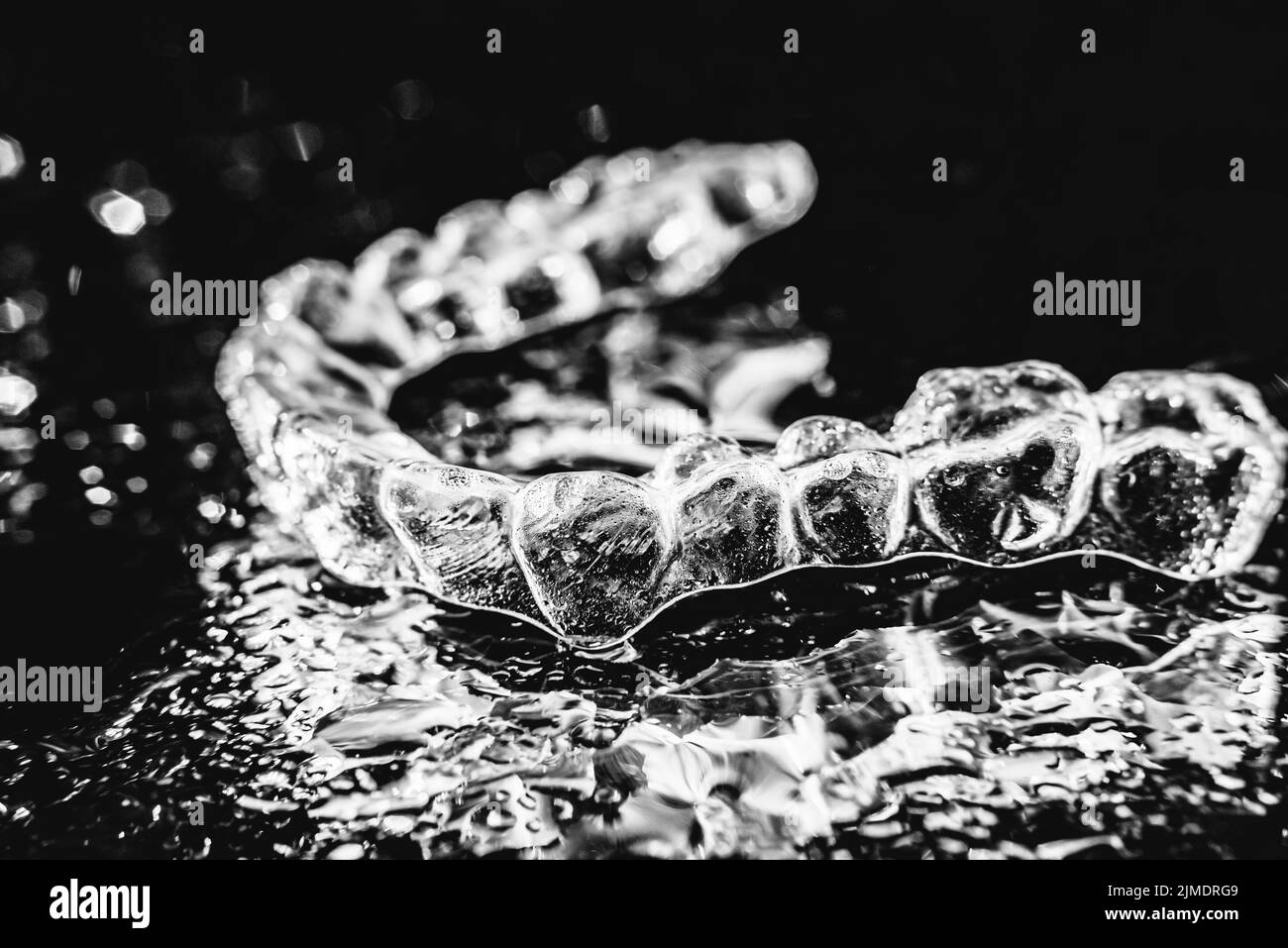 Transparente Ausrichter, Zahnhalter liegen auf Glas mit Wassertropfen auf schwarzem Hintergrund Stockfoto