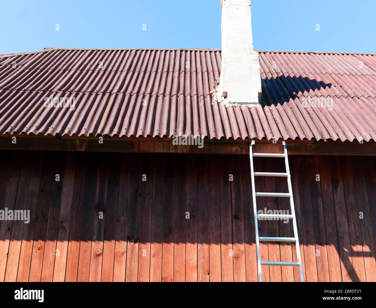 Eine Stahlleiter, die gegen das Dach gelehnt ist, und ein Kamin muss repariert werden Stockfoto
