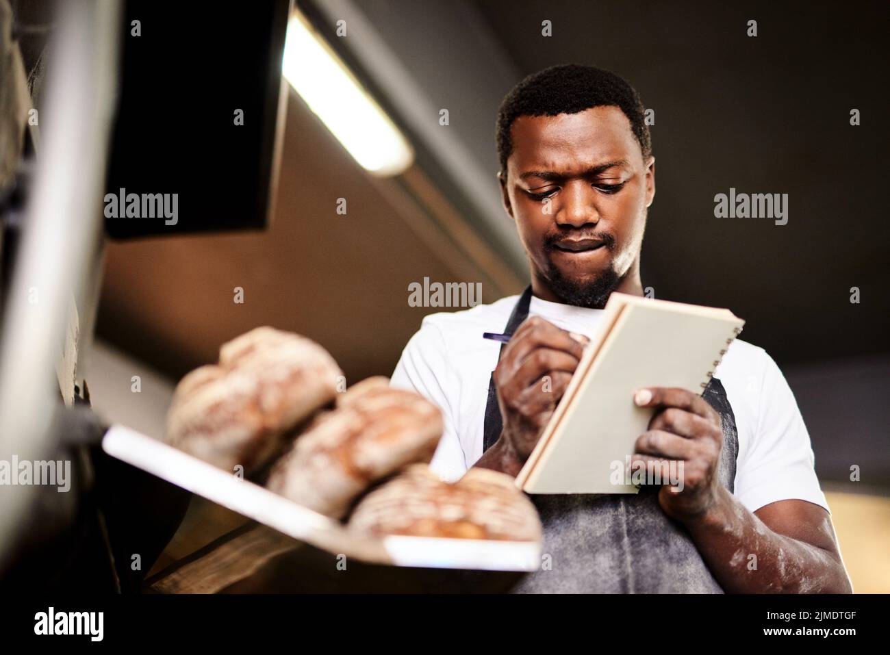 Jetzt bin ich auf halbem Weg durch meine Bestellliste. Ein männlicher Bäcker macht sich Notizen, während er in seiner Bäckerei arbeitet. Stockfoto