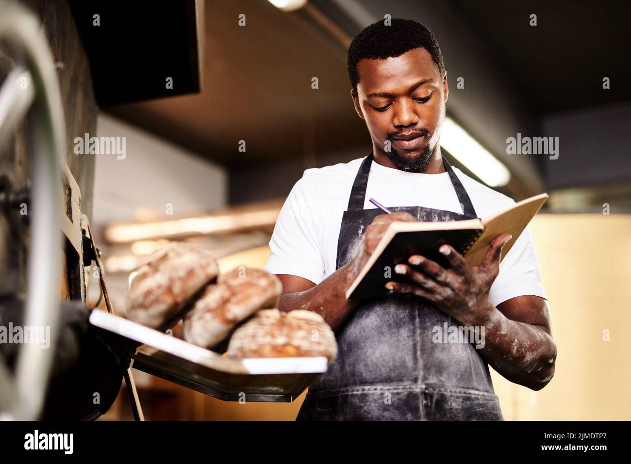 Ich probierte ein neues Rezept aus und musste einige Änderungen vornehmen. Ein Bäcker machte sich Notizen, während er in seiner Bäckerei arbeitete. Stockfoto