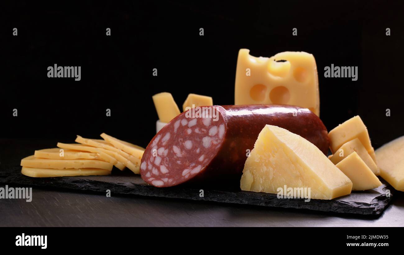 Mehrere Käsesorten und ein Stück Salami-Laib befinden sich auf einem schwarzen Steinbrett. Stockfoto