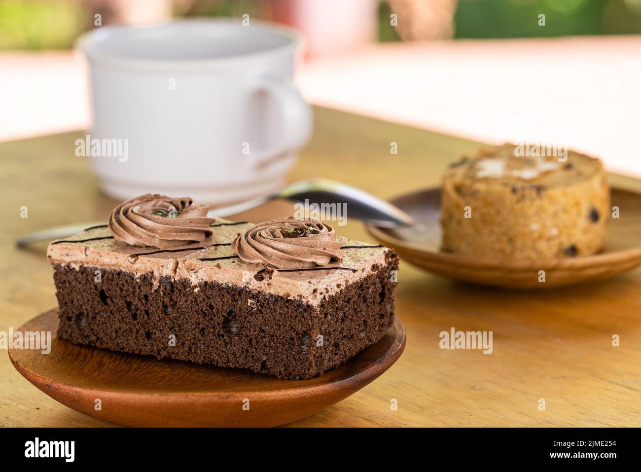 Mini-Schokoladencreme-Biskuitkuchen in Holzplatte und Stück Prune-Biskuitkuchen in Holzschale mit einer Tasse Kaffee. Stockfoto