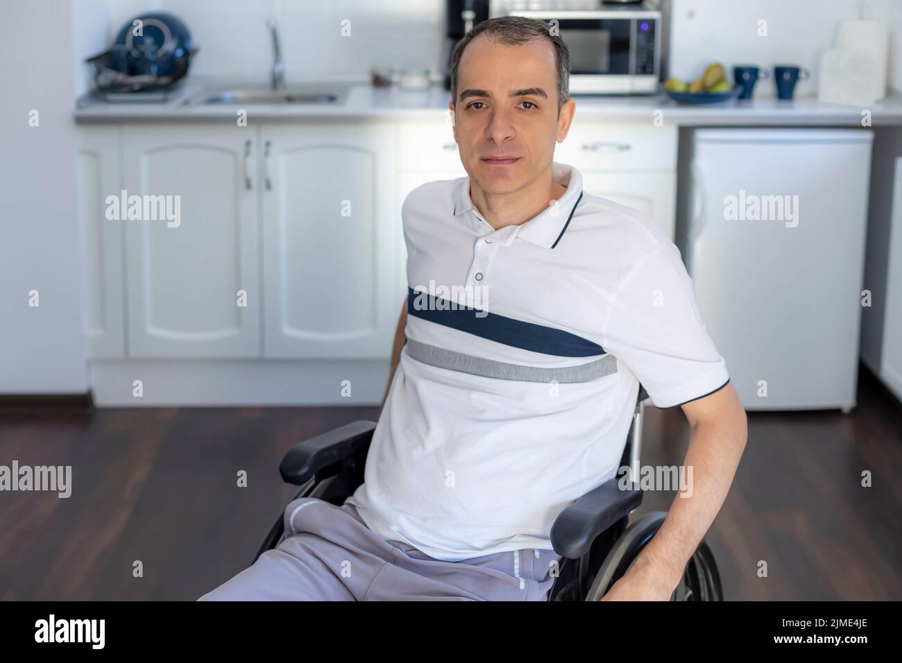Lächelnden jungen Behinderten Mann sitzt im Rollstuhl In der Küche Stockfoto Lächelnden jungen Behinderten Mann sitzt im Rollstuhl In der Küche Stockfoto
