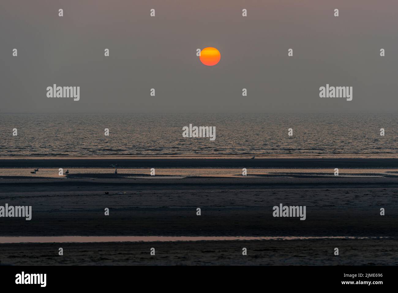 Orangefarbener Sonnenuntergang über dem Meer vom Strand aus gesehen Stockfoto