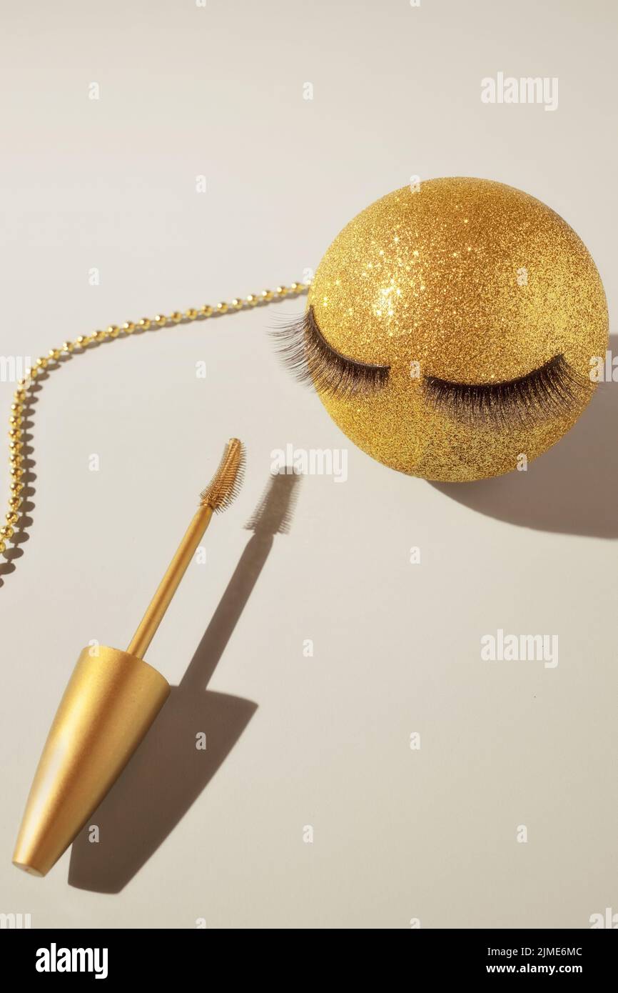 Mascara und ein goldener Weihnachtsball mit falschen Wimpern. Das Konzept der festlichen Make-up für Frauen. Stockfoto