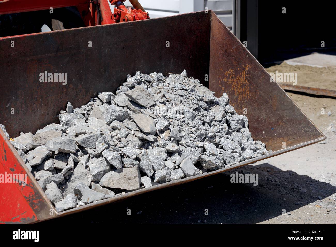 Entfernung von Bauschutt. Der Eimer des Traktors ist mit Betonschutt und Pflasterplatten gefüllt. Stockfoto