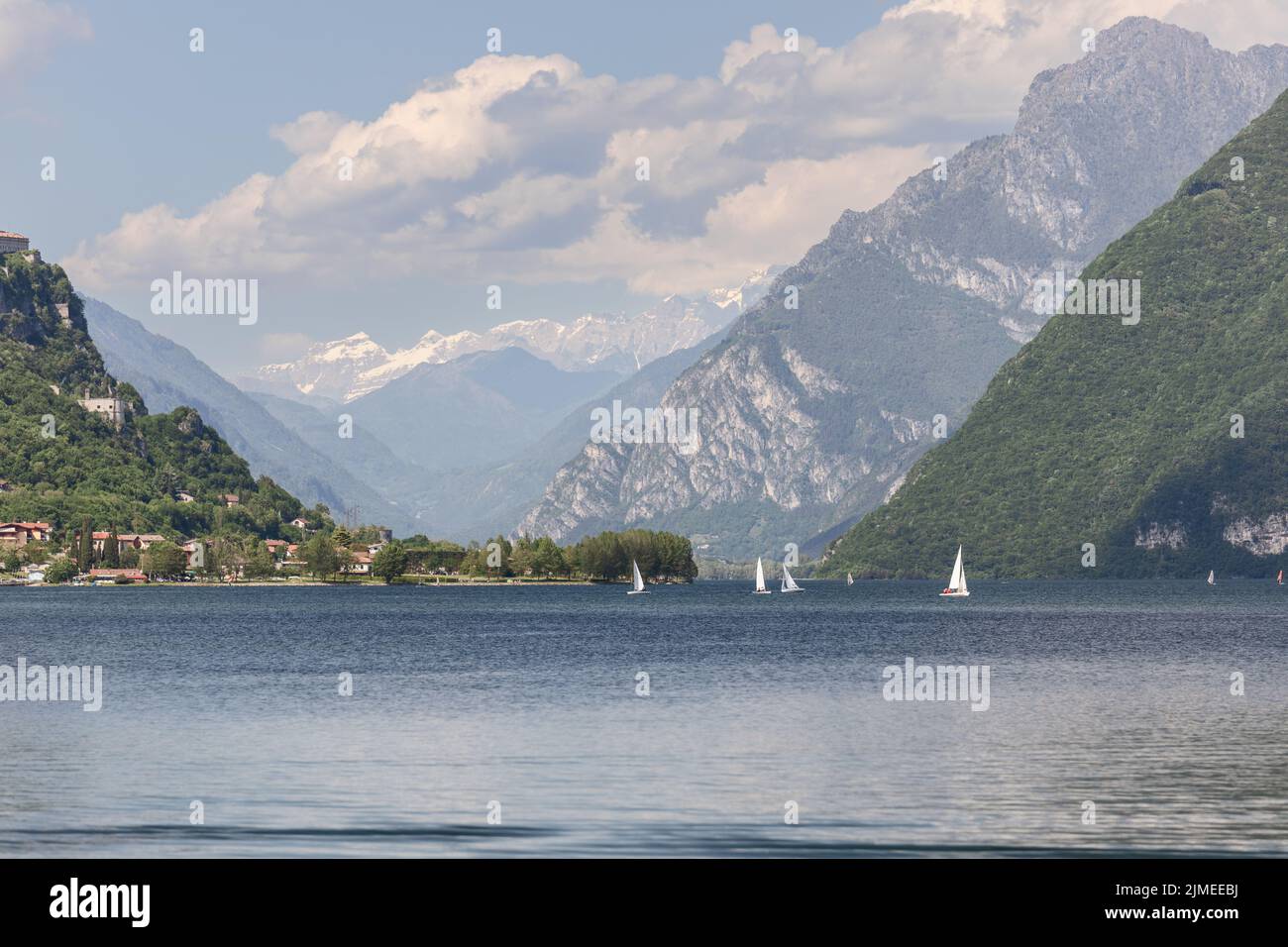 Segelboote überqueren das Wasser eines alpinen Sees Idro (Lago d'Idro), umgeben von felsigen grünen, bewaldeten Bergen, die sich über den Horizont erstrecken. Brescia Stockfoto