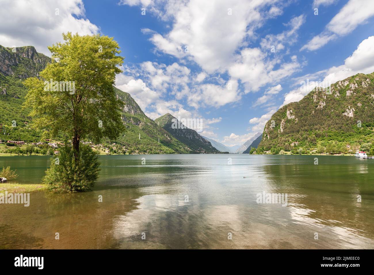 Das transparente, ruhige Wasser eines alpinen Idro-Sees (Lago d'Idro) reflektiert den Himmel umgeben von bergigen felsigen, bewaldeten Massifen Stockfoto