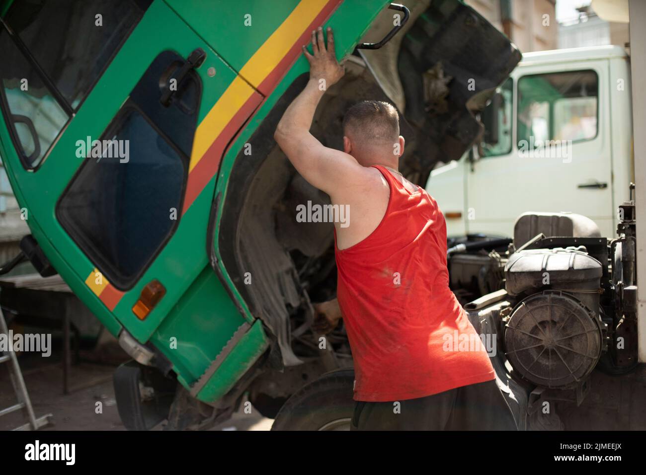 Fahrer repariert Stapler. Der Fahrer hebt die Kabine des Staplers an. Großes Auto. Typ in rotem T-Shirt. Stockfoto